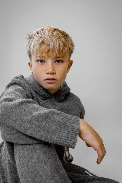 Jongen in grijze trui zit en kijkt in de camera